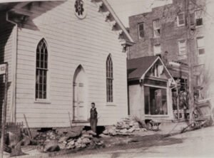 Black an dwhite image of church building with a man and building materials in front