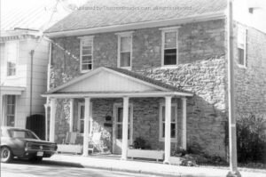 Black and white image of brick building with triangular awning over front door