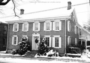 Black and white photo of brick house with snow on roof and ground