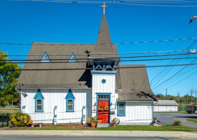 Front view of church house. White paneling, blue windows, and steep roof.